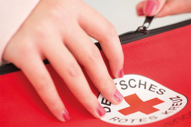 Foto: Eine Frau öffnet eine rote Tasche mit DRK-Rundlogo als Aufdruck.